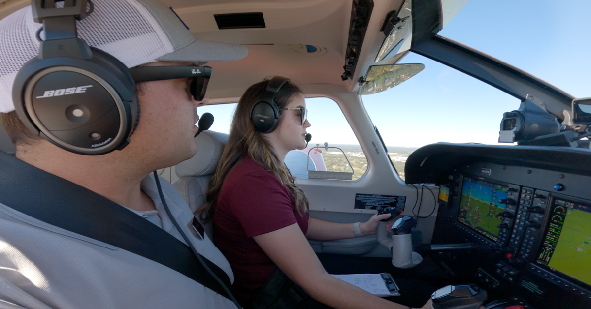 Profile view of Certified Flight Instructor and pilot training in-flight. Image shows both inside Piper Archer aircraft with controls and landscape visible.