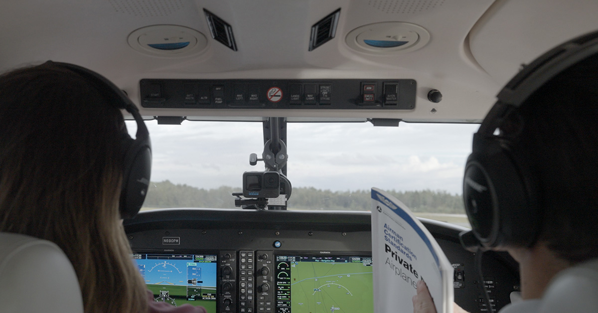 View inside aircraft showing ground school student and flight instructor holding reference book