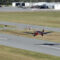 Piper Archer landing at small rural airfield with wind sock, other aircraft, and taxiway visible