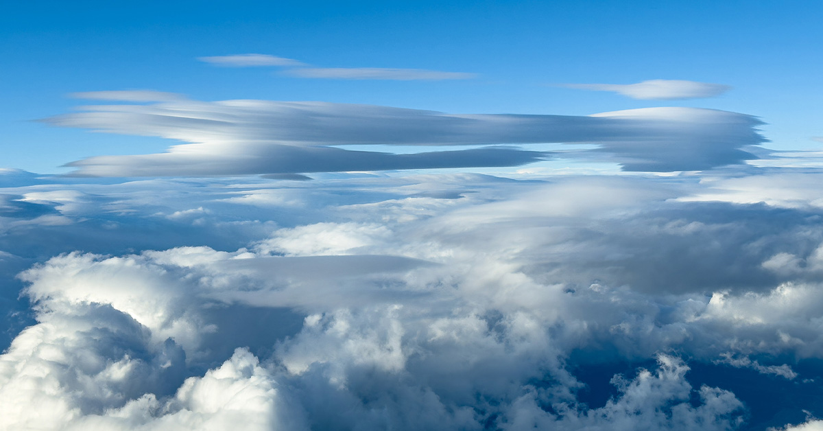 Expansive aerial landscape with dramatic lenticular cloud above distant mountains and valleys displaying cloud layers at varying altitudes and temperatures