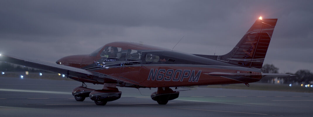 Piper Archer aircraft on taxiway at dusk with aircraft and runway lights visible
