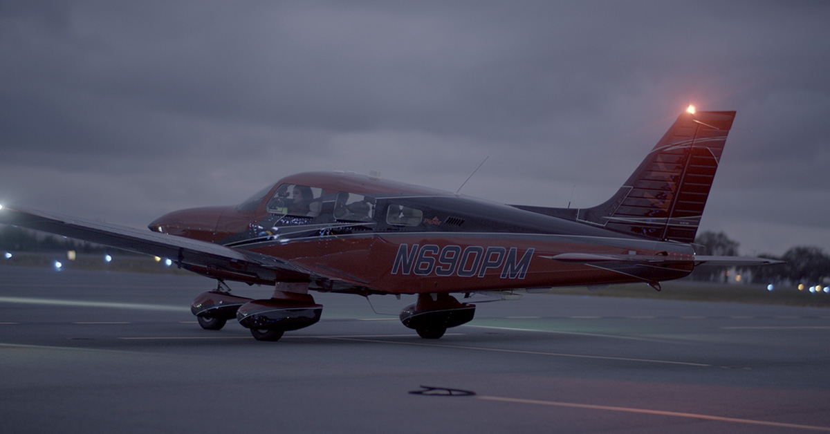 Piper Archer aircraft on taxiway at dusk with aircraft and runway lights visible
