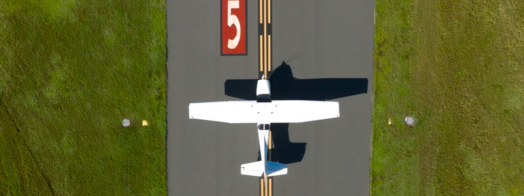 Aerial views of white aircraft on taxiway at small airfield