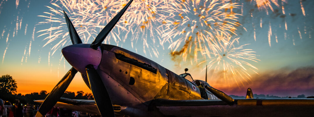 Fireworks light up the sky behind a grounded Spitfire