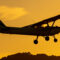 Silhouette of small propeller plane landing or taking off on the runway backlit under a yellow sun with the mountain below at sunset