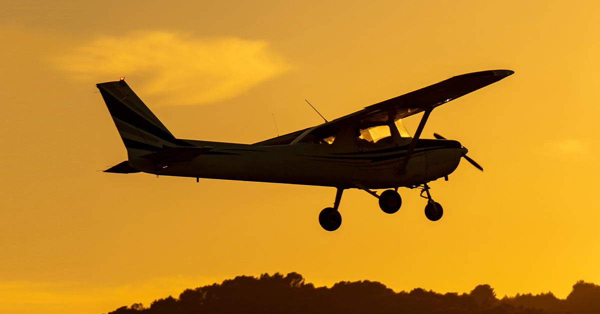 Silhouette of small propeller plane landing or taking off on the runway backlit under a yellow sun with the mountain below at sunset
