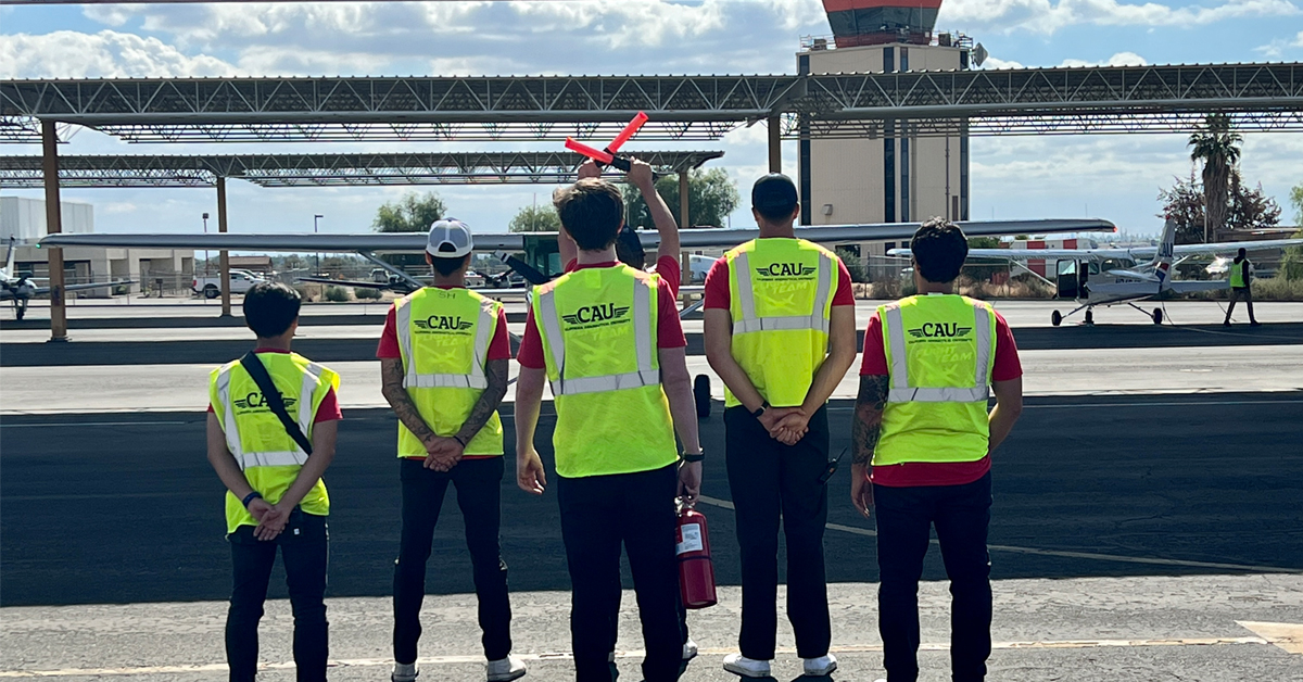 Five CAU student pilots in yellow vests on runway