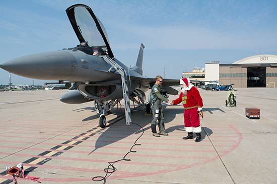 Santa shaking hands with a fighter pilot in front of a fighter jet.