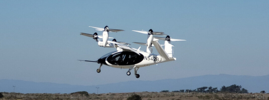 An experimental eVTOL aircraft above runway during take-off with mountains behind.