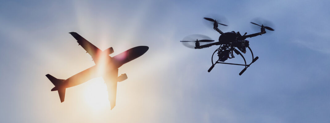 Drone and airplane together in the sky with sun in back.