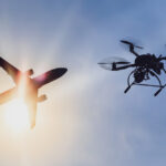 Drone and airplane together in the sky with sun in back.