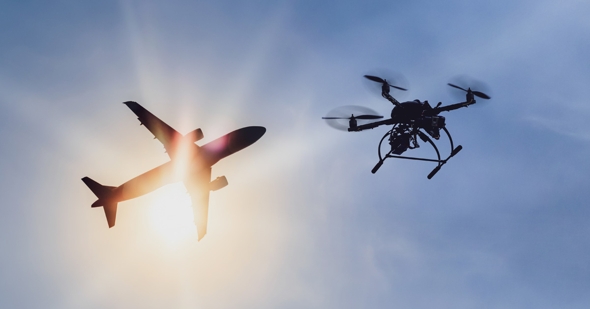 Drone and airplane together in the sky with sun in back.